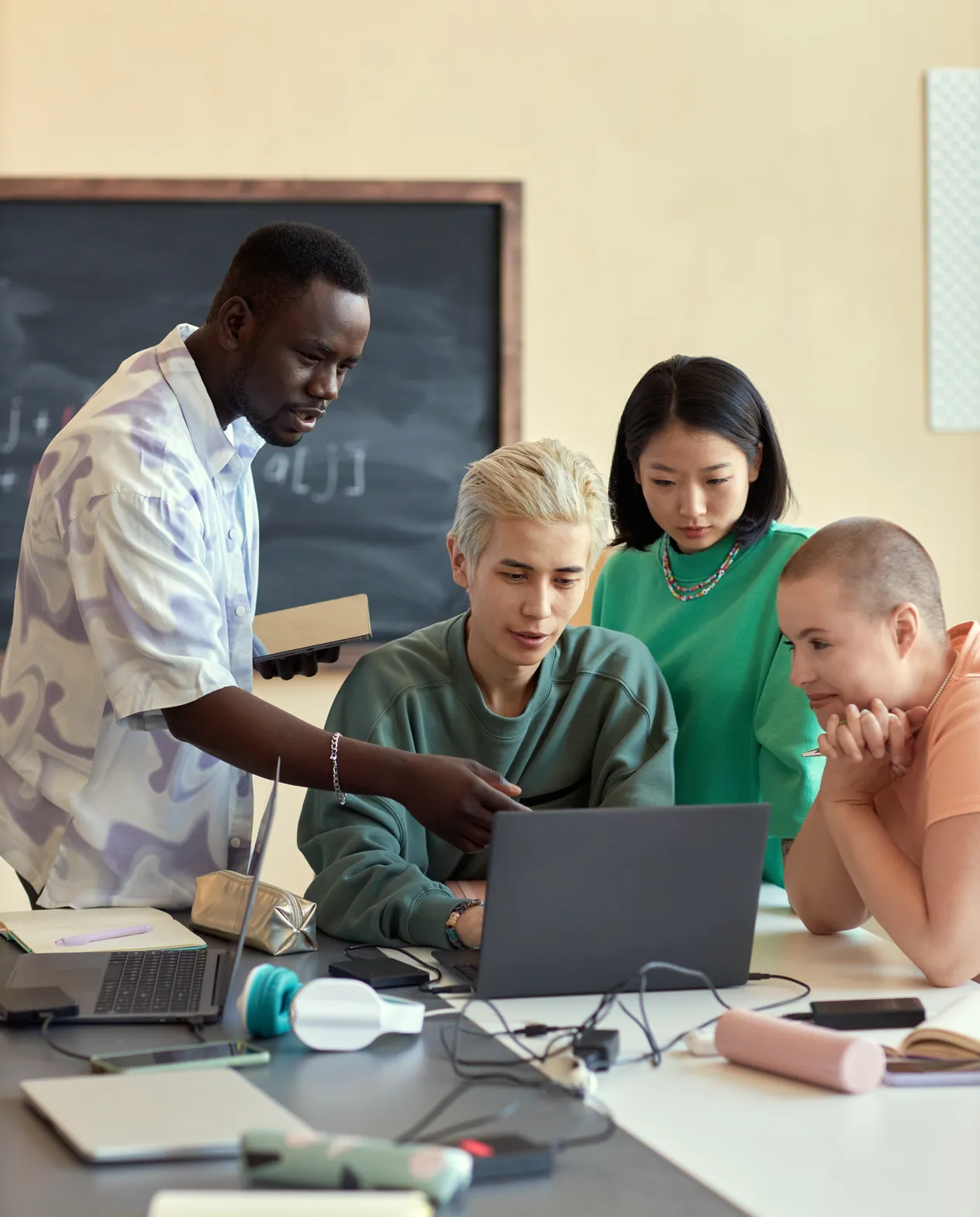 Someone leaning in to point at a laptop screen for three colleagues gathered round it, a chalkboard behind them